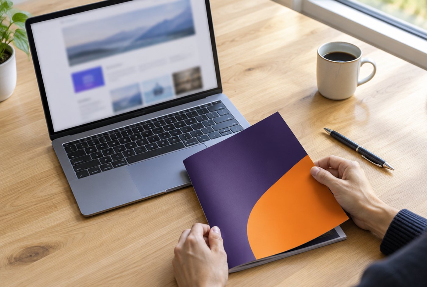Sur un bureau : ordinateur portable, plaquette commerciale violette et orange, carnet